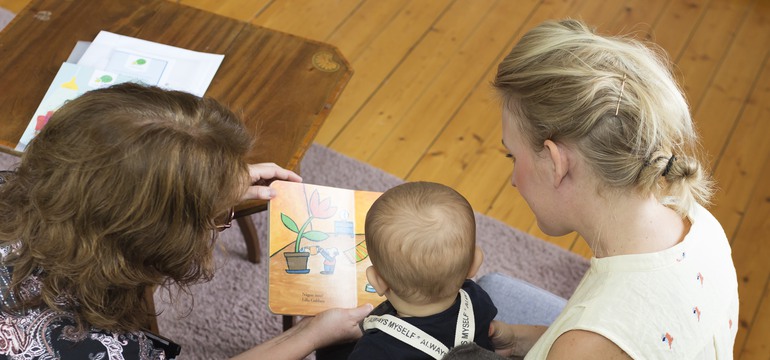 Två vuxna läser bok tillsammans med ett litet barn